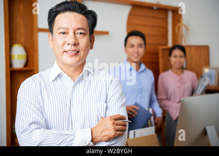 Portrait von Reifen zuversichtlich Vietnamesischen Unternehmer steht mit seinen Armen in Unternehmen Office gekreuzt Stockfoto
