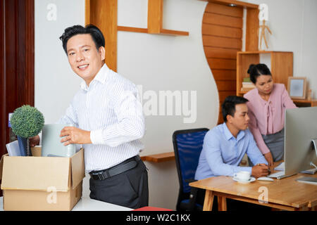 Fröhliche reife asiatischer Mann seine Sachen aus Karton am neuen Arbeitsplatz im Büro Stockfoto