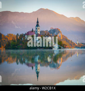 Die Insel (Blejski otok) mit der Kirche Mariä Himmelfahrt (Cerkev Marijinega vnebovzetja) & Burg von Bled beleuchtet bei Sonnenaufgang, der See von Bled, Bled, Obere Krain, Julische Alpen, Slowenien Stockfoto