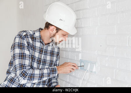 Der master Reparaturen die Buchse mit einem Schraubendreher zum Einbau in die Wand. Stockfoto