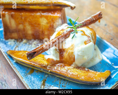 Vanille Eis topping mit Karamell auf Keramikplatte auf hölzernen Tisch. Close-up karamellisierten Bananen Toast hausgemachter Nachtisch. Stockfoto