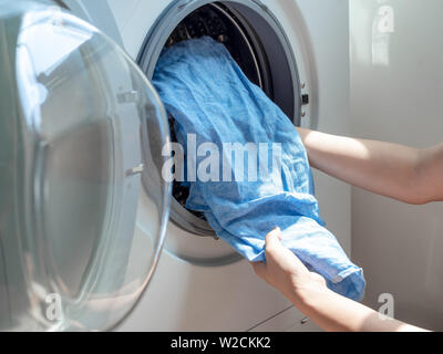 Close-up Woman's Hand schmutzig Blau Leinen Shirt in der Waschmaschine. Stockfoto