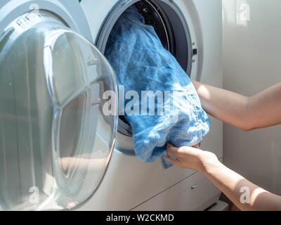 Close-up Woman's Hand schmutzig Blau Leinen Shirt in der Waschmaschine. Stockfoto