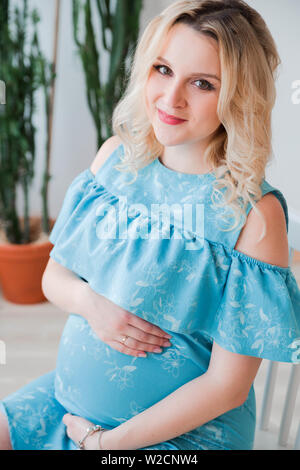 Foto der schwangeren Frau in einem blauen Kleid umarmt sie Bauch Stockfoto