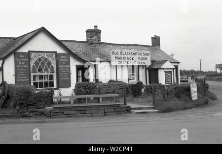 1950er Jahre, historisch, Außenansicht des Old Blacksmith's Shop, Gretna Green, Schottland. Seit 1754 ist es ein Veranstaltungsort für Hochzeiten und berühmt für seinen "Marriage Room", der sogenannte "Runaway Ehen" hielt, da sich das schottische Recht von dem in England Unterschied, wo man 21 Jahre alt sein und in einer Kirche heiraten musste. In Scotand konnte man vor Ort heiraten, in einer einfachen "Ehe durch Erklärung, nur zwei Zeugen und Zusicherungen von dem Paar, dass sie beide frei zu heiraten und da Gretna war kurz über der Grenze von England, viele taten. Erbaut 1713, liegt es an der Kreuzung von fünf alten Poststrassen. Stockfoto