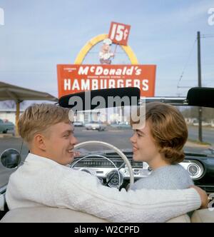 Fast food in den 1950er Jahren. Ein junges Paar in ihrem Cabrio mit einem McDonald's Schild im Hintergrund. Die gelbe Bogen, die Teil des ursprünglichen Design bezeichnet die goldenen Bögen wurde erstmals 1953 verwendet. Die Kosten für eine begrenzte Speisekarte hamburger, schütteln und Pommes frites war 15 Cent. 1950er Jahre 1960er Jahre ref 5-40-4 Stockfoto