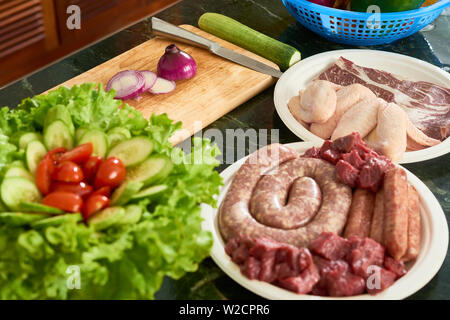 In der Nähe von frischem rohem Rindfleisch und Huhn Fleisch auf dem Teller mit Salat und Gemüse auf dem Tisch in der Küche Stockfoto