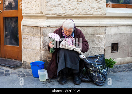 Lemberg, Ukraine - 26. Mai 2019: ältere Frau, die Blumen. Alte Frau sitzt auf der Straße und lesen Zeitung Stockfoto