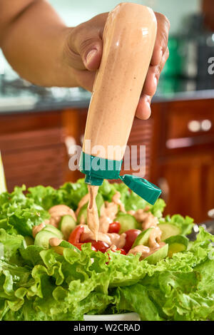 Nahaufnahme der Mann hält eine Flasche Sauce in seiner Hand und Hinzufügen in Gemüsesalat mit Salat und Tomaten Stockfoto