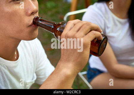 Close-up junger Mann mit Flasche und trinken Bier im Freien, während sitzen zusammen mit seinen Freunden Stockfoto