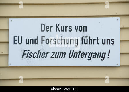 05 Juli 2019, Mecklenburg-Vorpommern, Freiesten: In den Hafen, ein Schild mit den Worten "den Kurs der EU, und die Forschung führt uns die Fischer zu ruinieren' hängt an der fischerhütte von einem Fischer aus den Freiesten Fischereigenossenschaft. Der Bundesminister für Ernährung und Landwirtschaft Klöckner mit Mecklenburg-Vorpommerns Landwirtschaftsminister Backhaus und Angeln Verbände am 8. Juli 2019 zu Gesprächen über Fangquoten 2020, sofortige Maßnahmen auf Dorsch in der Ostsee und die Fangmengen in der Sportfischerei. In Sassnitz-Mukran auf der Insel Rügen, der Minister visits einer der europaweit größten Fisch Stockfoto