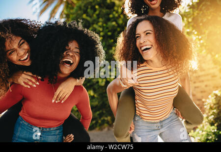 Freundliche weibliche Freunde wandern draußen in der Stadt und haben Spaß. Junge Frauen ihren Freunden draußen in der Stadt huckepack. Stockfoto