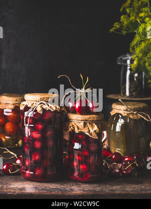 Ernte erhalten. Gläser mit caned Kirschen Kompott auf dunklen rustikalen Küche Tisch mit anderen für für den Winter zu konservieren. Canning und Gestalteri Stockfoto