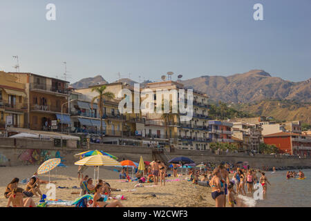 Giardini Naxos Sizilien Italien 2019 Blick auf den beliebten Strand überfüllt von Touristen und Menschen, die Gebäude entlang der Straße mit Blick auf das Meer Stockfoto