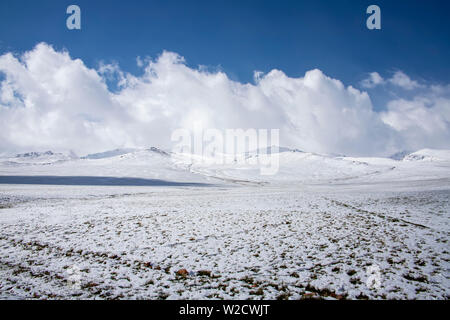 Blick auf den verschneiten Wiesen und Hügel gegen den Himmel mit Wolken. Das Reisen in Kirgistan. Stockfoto