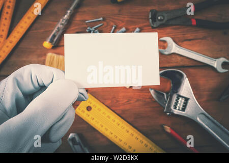 Haus Bau und Reparatur Dienstleistungen Mitarbeiter Holding blank Business Card über die Arbeit Tools auf Holz- Hintergrund Stockfoto