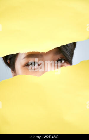 Portrait von Asiatische junge Frau versteckt sich hinter der gelben Papier und zeigt nur ihre schönen braunen Augen und Kamera Stockfoto