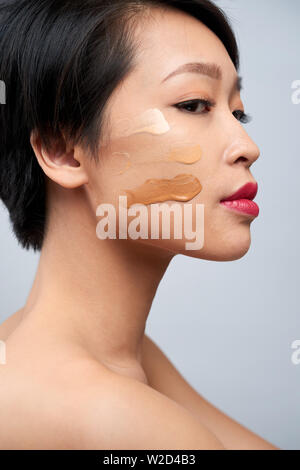 Seitenansicht des Asiatischen junge Frau mit dunklen kurzen Haaren in verschiedenen Farben der Stiftung für Gesichts-Make-up Stockfoto