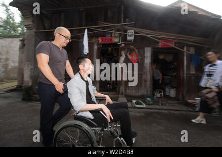 (190708) - LINHAI, Juli 8, 2019 (Xinhua) - Wu Yuanmiao auf einem Rollstuhl wird von Zhang Hailin auf dem Weg zu einer öffentlich-rechtlichen Tätigkeit in Linhai Stadt geschoben, der ostchinesischen Provinz Zhejiang, 27. Juni 2019. Wu Yuanmiao, beim Arbeiten als ein Friseur, ein Regelsatz für sich kostenloser Service ein Tag in der Woche an die Alte, Behinderte, und Soldaten. Mit mehr als 60.000 Kunden für 17 Jahr diente, ist er der Gewinner zahlreicher Auszeichnungen, darunter 1. Mai Arbeit Medaille. Aber bestimmt mit Erkrankungen des Gehirns, Wu's Zustand schlechter seit 2008 wurde. Im Jahr 2014 erlebte er eine harte Zeit in seinem Betrieb Stockfoto