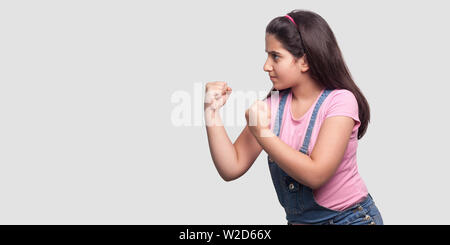 Profil Seitenansicht Portrait von schweren oder wütenden jungen Mädchen in rosa t-shirt und blauen Overalls stehen mit den Fäusten boxen Hände und bereit zum Angriff. indo Stockfoto