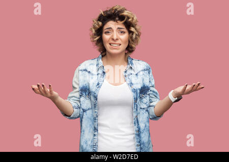 Was? Portrait von verwirrt oder junge Frau mit Curly Frisur im casual blaues Hemd stehend mit erhobenen Armen schockiert und Kamera besorgt. Ich Stockfoto
