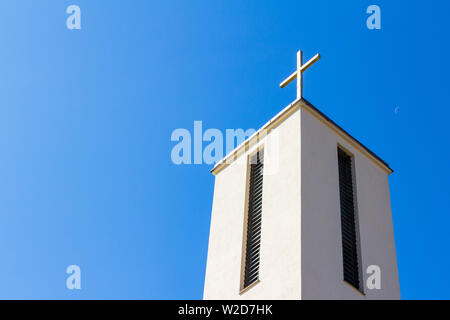 Leuchtendes Kreuz oben auf dem Kirchturm von St. Stephan Kirche gegen den blauen Himmel und Halbmond in Sopron, Ungarn Stockfoto