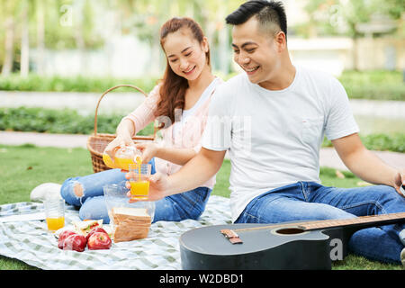 Asiatische junge Frau gießen Orangensaft in der man Glas und sie ruht auf frische Luft beim Picknick im Park Stockfoto
