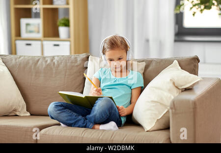 Mädchen in Kopfhörer mit Tagebuch auf dem Sofa zu Hause Stockfoto