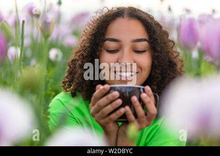 Gemischte Rasse schöne Afrikanische Amerikanische biracial Mädchen Teenager weibliche junge Frau trinkt Tee oder Kaffee, der eine grüne T-Shirt in Rosa Stockfoto