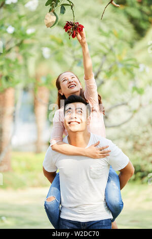 Schöne asiatische Frau ihre Hand bis zu den Blumen auf dem Baum, während jungen Mann mit ihr, die Zeit im Freien Stockfoto