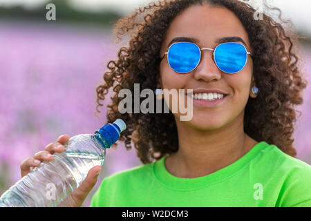Gemischte Rasse schöne Afrikanische Amerikanische biracial Mädchen Teenager weibliche junge Frau trägt blaue Sonnenbrille im Bereich der rosa und lila Blumen lächeln wi Stockfoto
