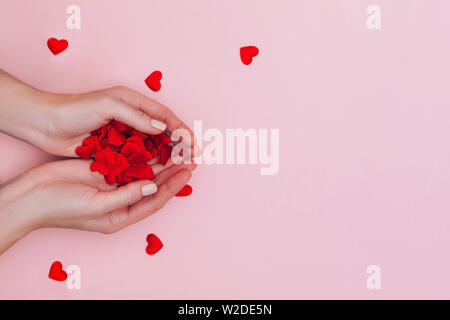 Die Frau Hände voll von kleinen roten Herzen auf rosa Hintergrund. Liebe, Fürsorge, Liebe, Tag Konzept der St. Valentin. Stockfoto