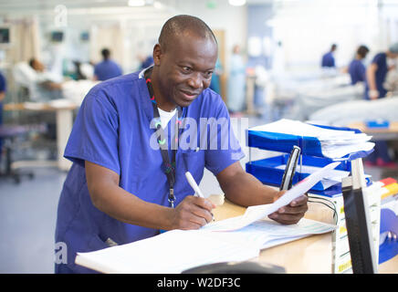 Männliche NHS Krankenschwester an einem Arbeitsplatz in einem Krankenhaus Umgang mit Patienten Hinweise und telefonische Anfragen. Stockfoto