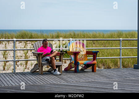 ATLANTIC CITY, NEW JERSEY - Juni 18, 2019: Ein Mann auf einer Bank am Rand von einem Holzsteg ruht. Stockfoto