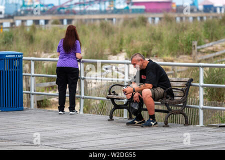 ATLANTIC CITY, NEW JERSEY - Juni 18, 2019: Ein Mann auf einer Bank am Rand von einem Holzsteg ruht. Stockfoto