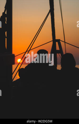 Paar auf einem Segelboot gegen pulsierenden Sonnenaufgang Silhouette Stockfoto