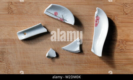 Gebrochene chinesische Suppe Löffel mit den Stücken auf einem hölzernen Fläche verstreut. Stockfoto