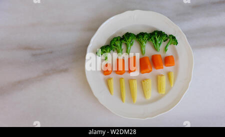 Anordnung von Brokkoli, baby Mais und Karotten, auf einer weißen Platte auf eine Marmorarbeitsplatte platziert. Stockfoto