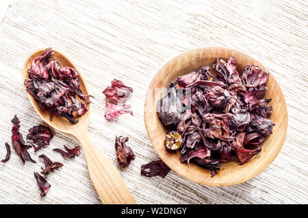 Ansicht von oben an der hölzernen Schüssel und Löffel von trockenen Hibiscus Blüten auf Leinen Hintergrund Stockfoto