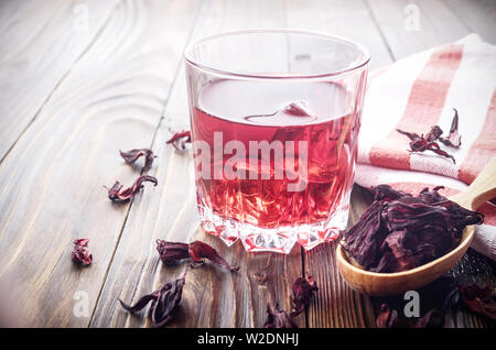 Detailansicht auf Glas Tee mit Eis und Löffel von trockenen Hibiscus Blüten auf hölzernen Tisch Hintergrund Stockfoto