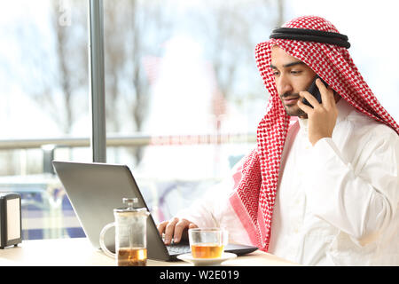 Arabischer Mann mit einem Laptop und dem Sprechen für snmart Telefon in einem Café sitzen Stockfoto