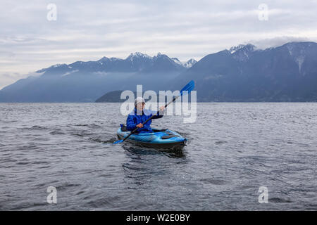 Abenteuerliche Menschen auf ein Kajak, Paddeln in Howe Sound bei einem bewölkten Abend. In der Nähe von Bowen Island, nordwestlich von Vancouver, BC, Kanada. Stockfoto