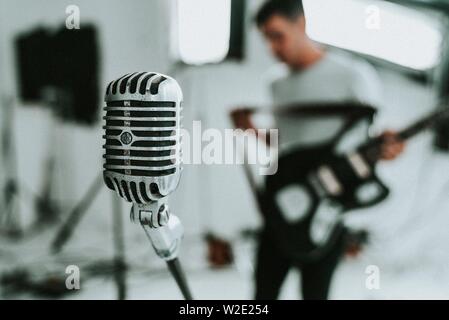 Kondensatormikrofon mit großer Membran und einem Musiker, der eine E-Gitarre hält Im Hintergrund Stockfoto