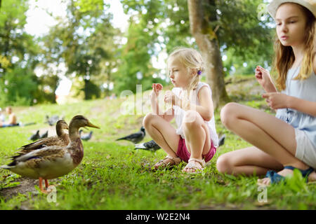 Zwei süße kleine Schwestern Fütterung Vögel auf Sommertag. Kinder füttern Tauben und Enten im Freien. Aktive Freizeit mit Kindern Stockfoto