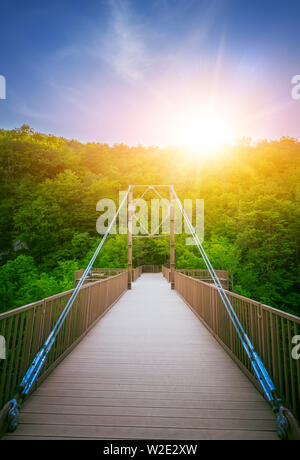 Die kleine Brücke über den Fluss und grüne Bäume auf einem hellen Sonnenuntergang Stockfoto