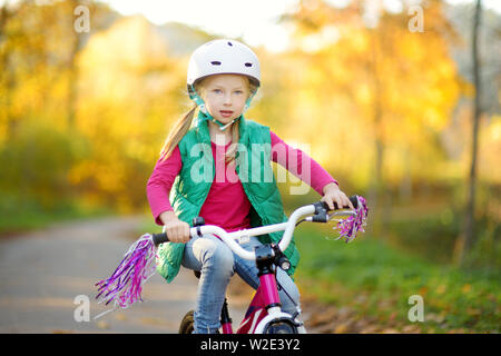 Süße kleine Mädchen mit dem Fahrrad in einem Stadtpark an sonnigen Herbsttag. Aktive Familie Freizeit mit Kindern. Kind tragen Helm beim Fahrrad fahren Stockfoto