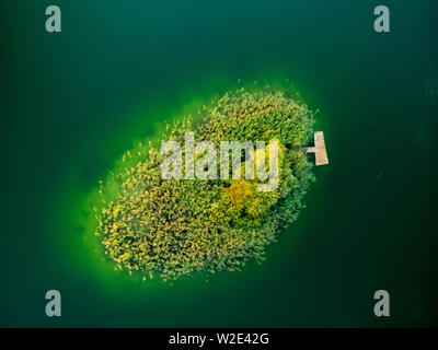 Luftbild von Oben nach Unten Blick auf einer kleinen Insel. Vögel Auge Ansicht der schönen grünen Wasser des Sees Gela umgeben von Pinienwäldern. Wolken reflektieren, Gela la Stockfoto
