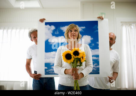 Porträt einer Mitte - erwachsene Frau mit einem Bündel Sonnenblumen vor wolkigem Himmel Hintergrund von zwei Männern. Stockfoto