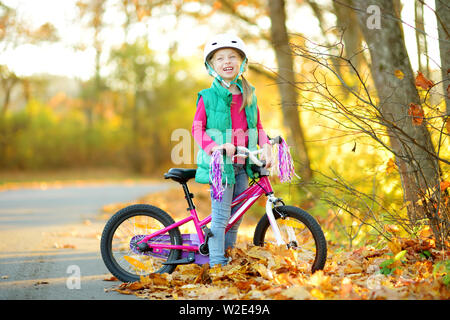 Süße kleine Mädchen mit dem Fahrrad in einem Stadtpark an sonnigen Herbsttag. Aktive Familie Freizeit mit Kindern. Kind tragen Helm beim Fahrrad fahren Stockfoto