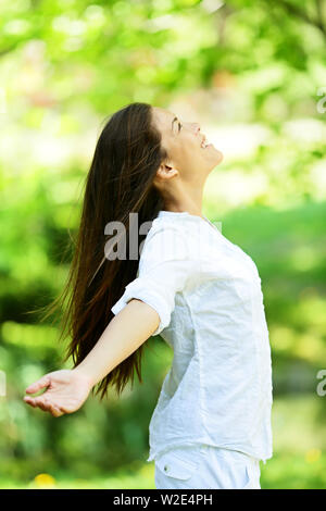 Junge Frau, die die Ankunft des Frühlings in einem grünen Park mit ausgebreiteten Armen und den Kopf in den Himmel erhoben, wie sie in der Natur freut sich. Freude und Freiheit Konzept. Stockfoto